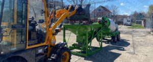 Compact wheel loader with pallet fork attachment displayed near storage containers and concrete mixing equipment
