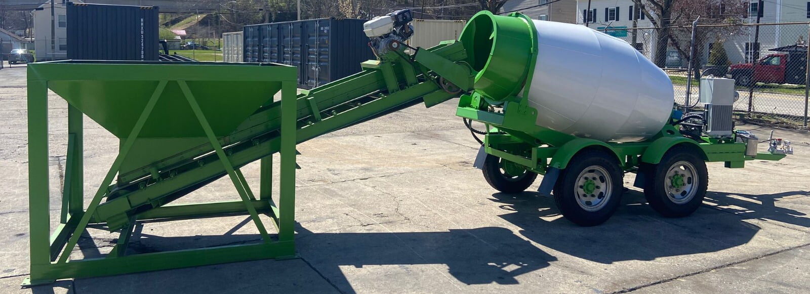 Concrete hopper loading a portable concrete mixer on trailer at a construction site.