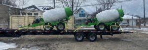 Two Ready Mixer concrete mixers with green and white drums secured on flatbed trailer in winter conditions